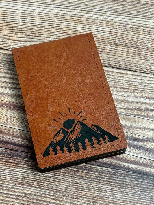 A folding cribbage board with a mountain design, closed and placed on a wooden surface.