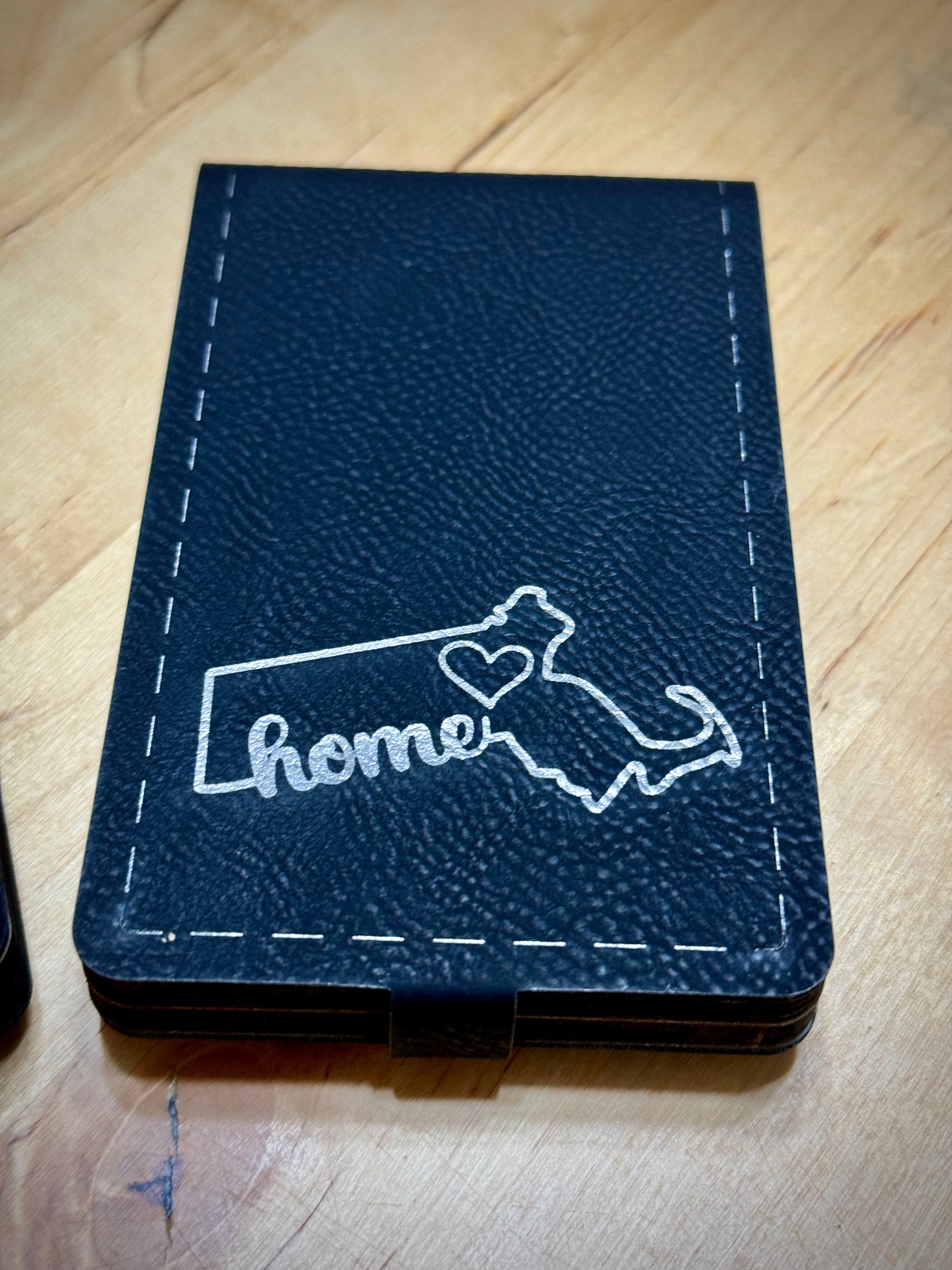 A folded cribbage board with a leatherette cover featuring a state-themed design and the word 'home' inscribed.