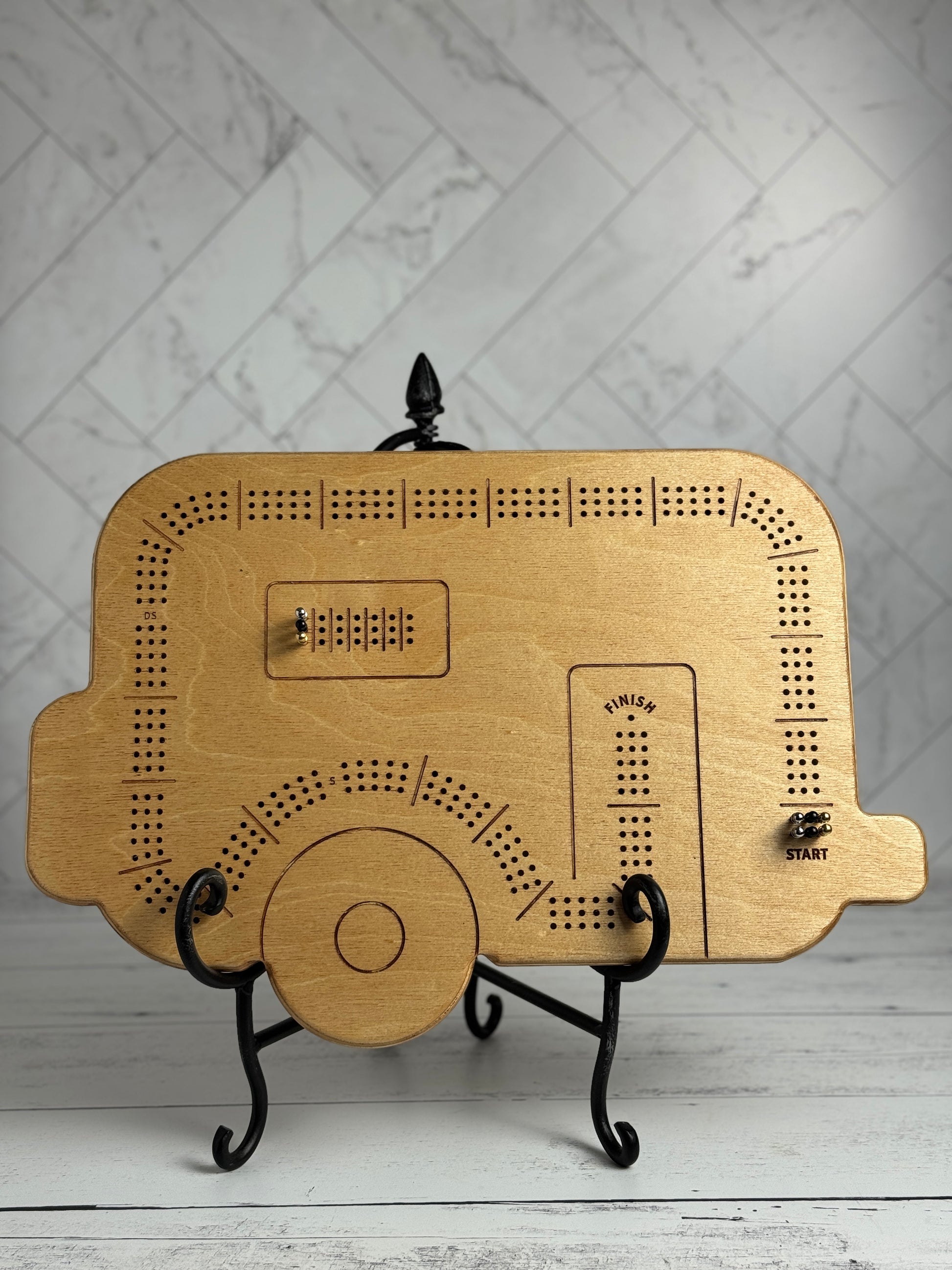 Travel trailer shaped wooden cribbage board with metal pegs against a white background