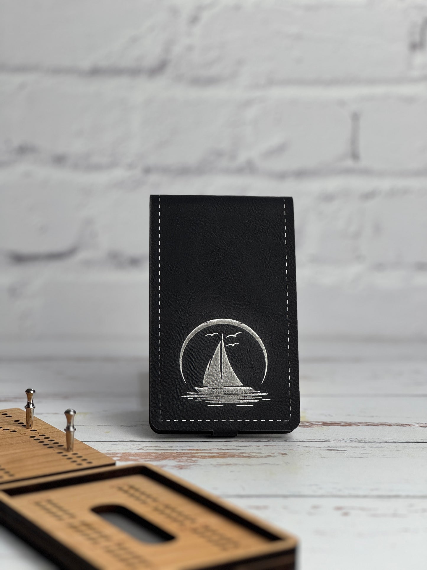 Black leather leatherette cribbage with sailboat design on a white wooden surface.