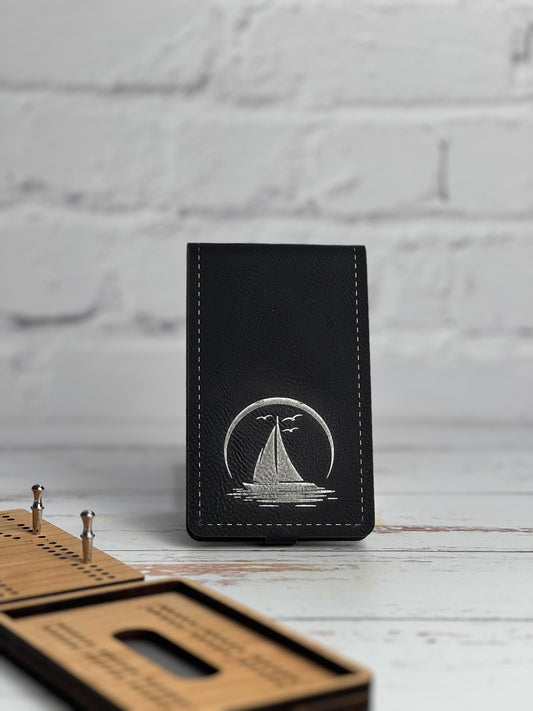 Black leather leatherette cribbage with sailboat design on a white wooden surface.