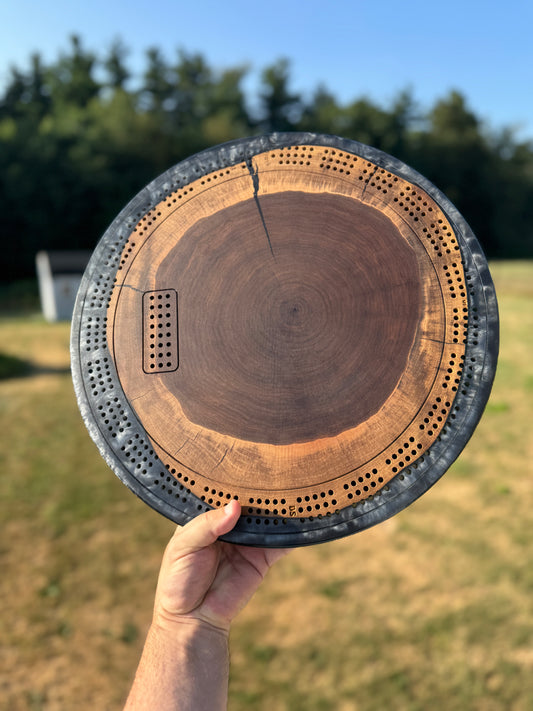 Eighteen inch round walnut cribbage board with grey resin held in front of a natural background