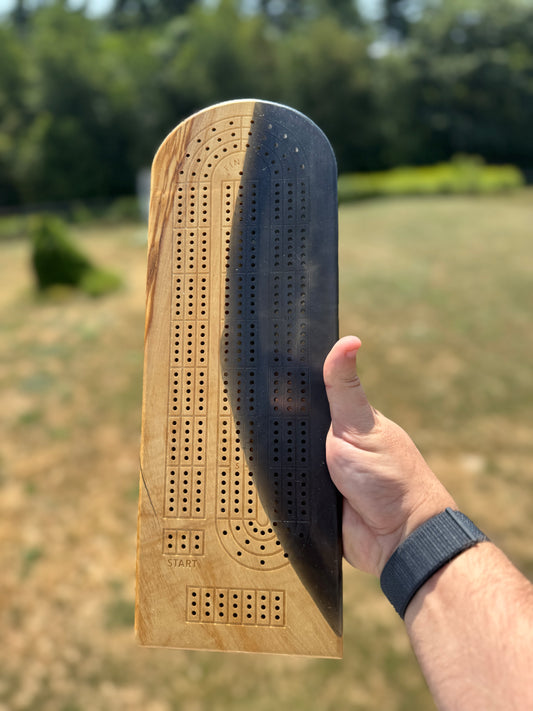 Rectangular cribbage board of olivewood and dark resin in a paperclip layout against a natural background.