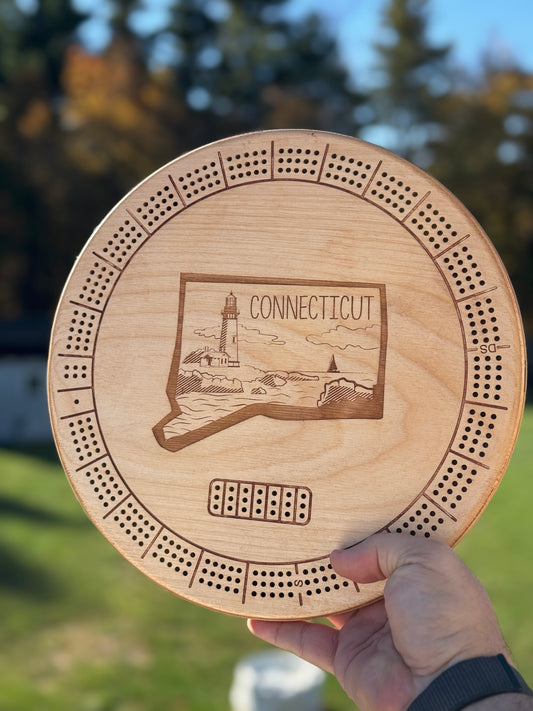 Round 3 track cribbage board with Connecticut state theme held against an outdoor backdrop